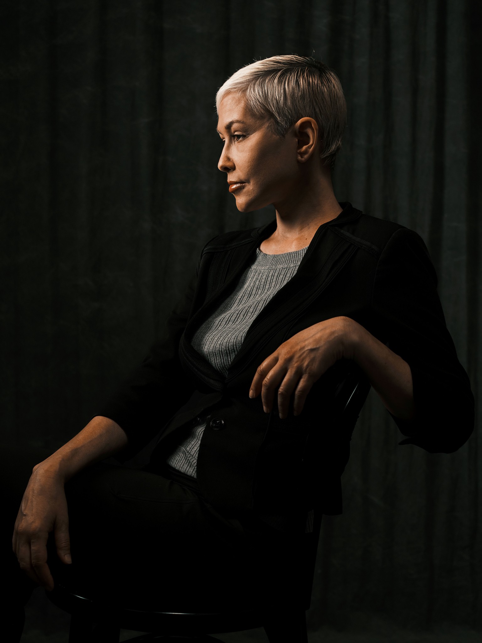Woman in profile seated against a dark studio backdrop.