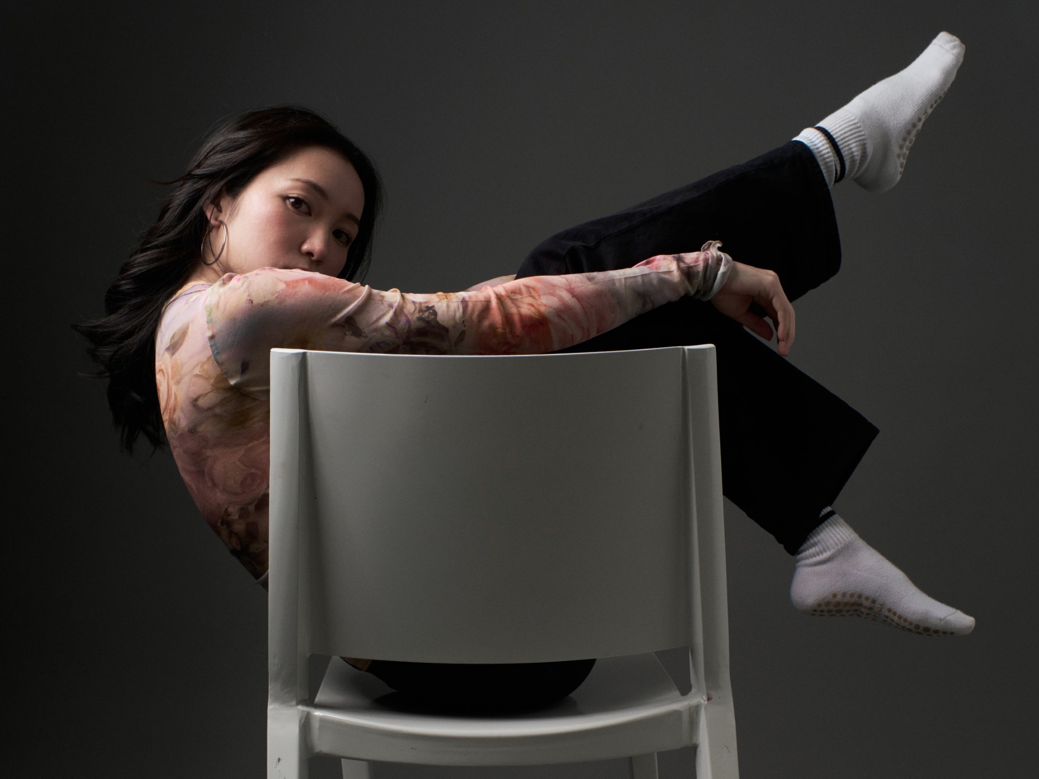 Woman posed sideways across a white chair against a dark studio background.