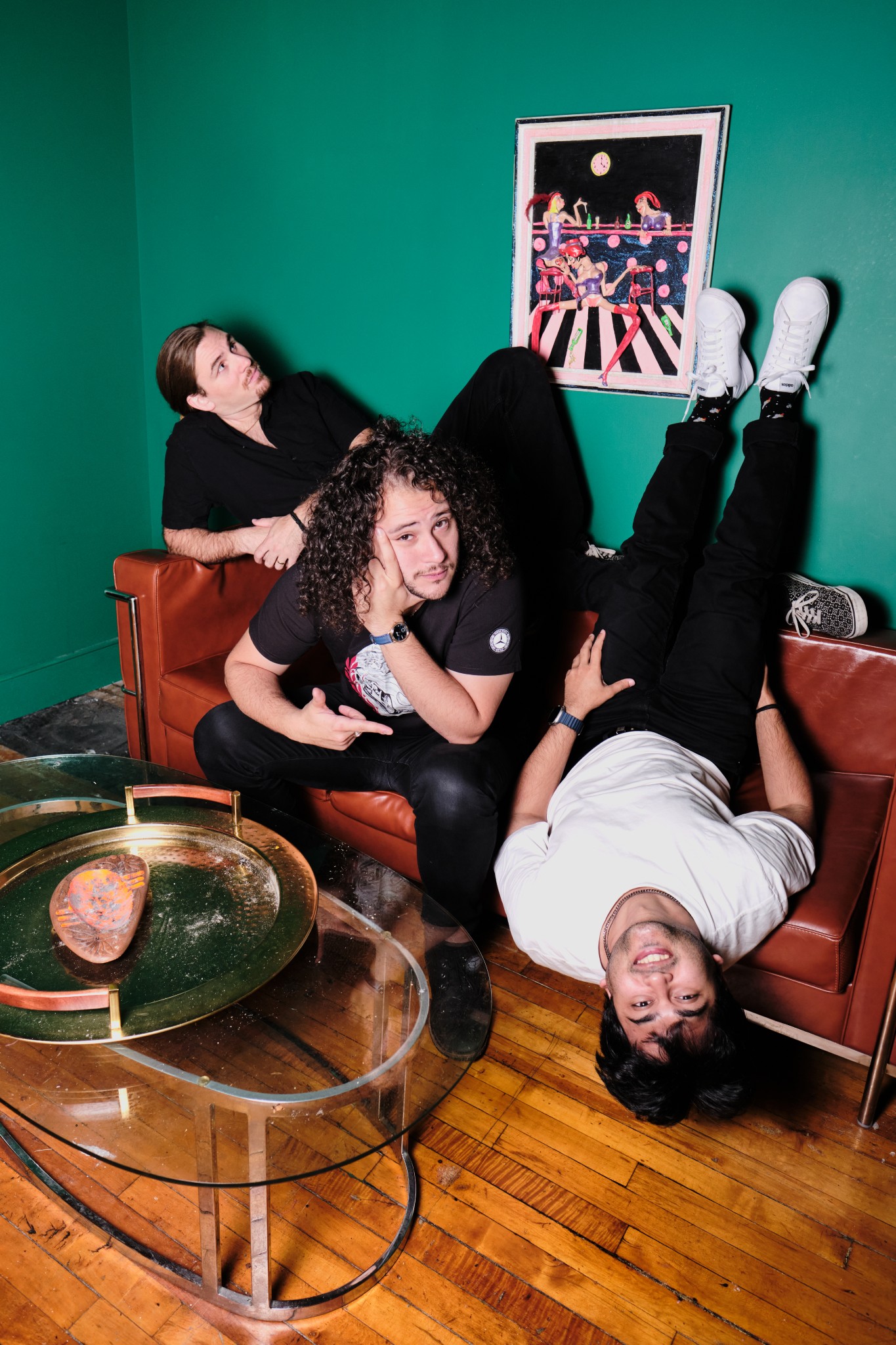 Four band members arranged playfully across a green room and leather sofa.